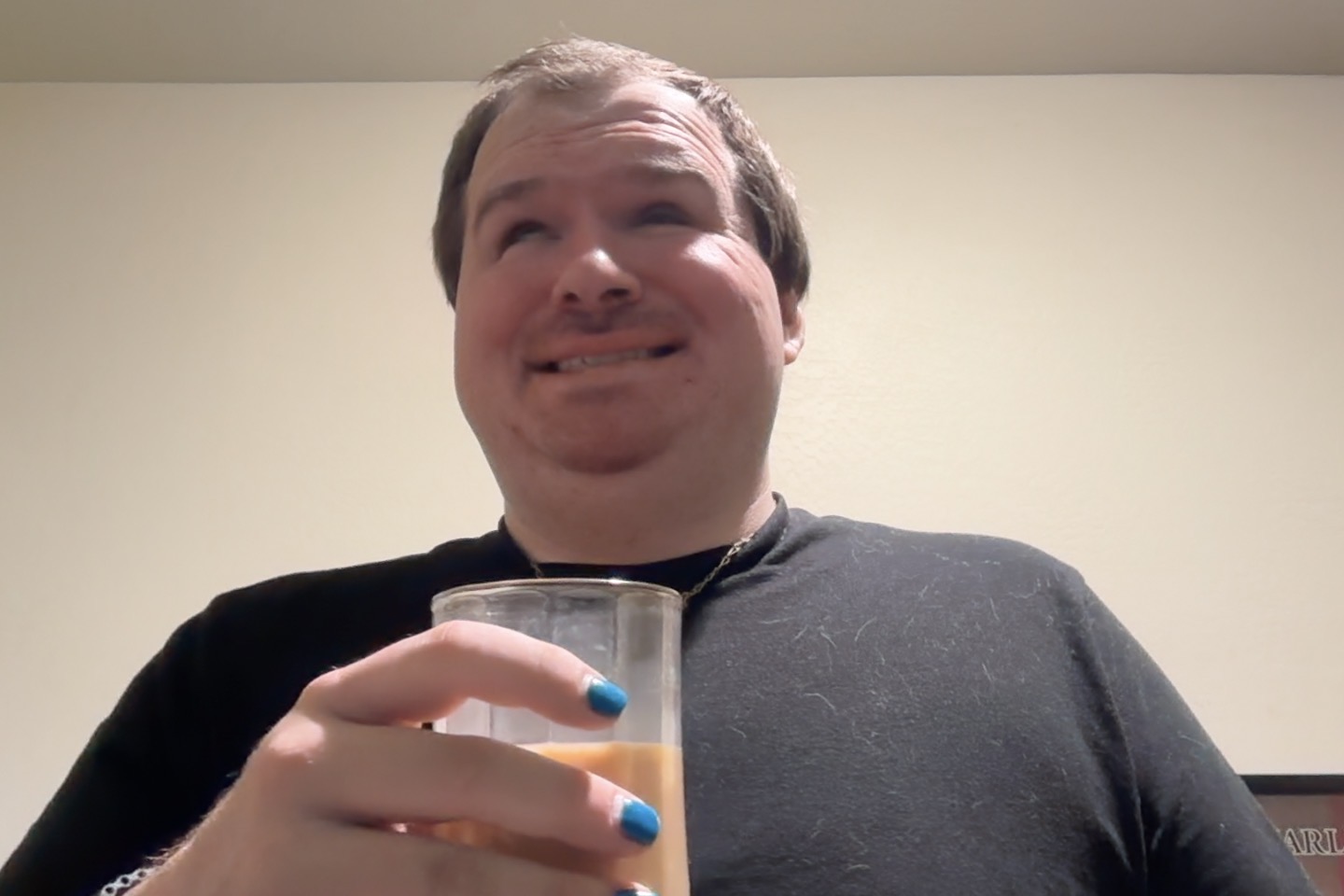 Blog for may 28th.jpg Tony, a smiling man with short hair, stands indoors holding a glass mug filled with coffee. He wears a black t-shirt, a gold necklace, and has teal blue nail polish on his fingernails. The background is a plain light-colored wall, and his expression is cheerful and relaxed.